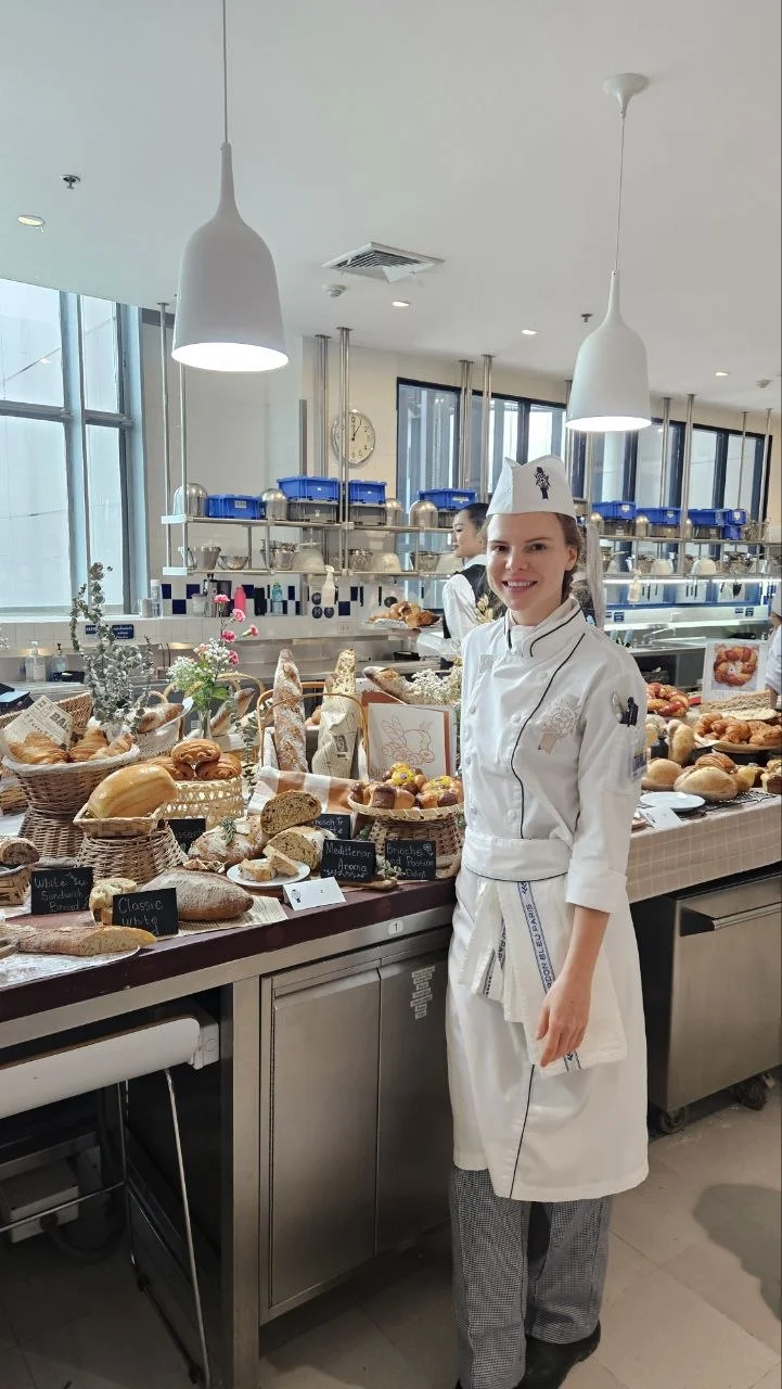 Lina in a chef uniform beside a display of bread in a teaching kitchen